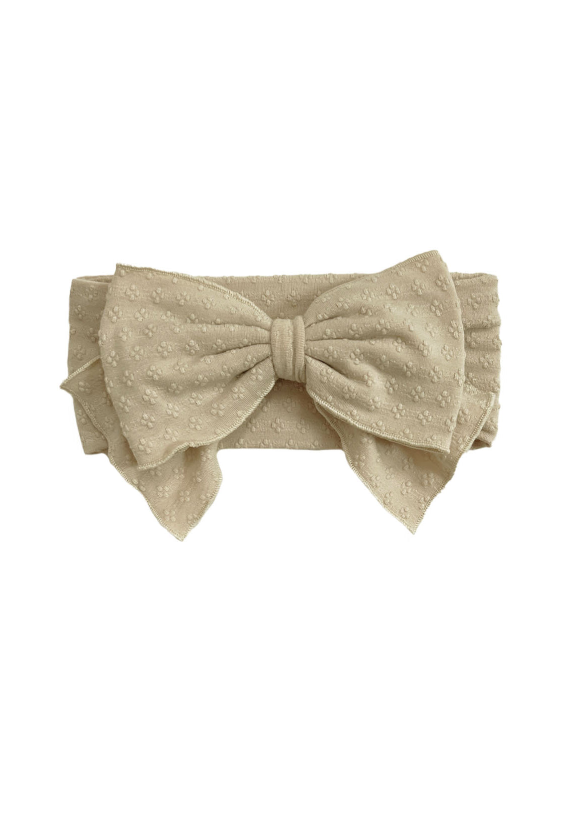 The Cinnamon Sugar Hair Accessory by Mabel and Honey is a beige fabric headband with a large bow and subtle textured floral pattern, adding elegant charm to any outfit.