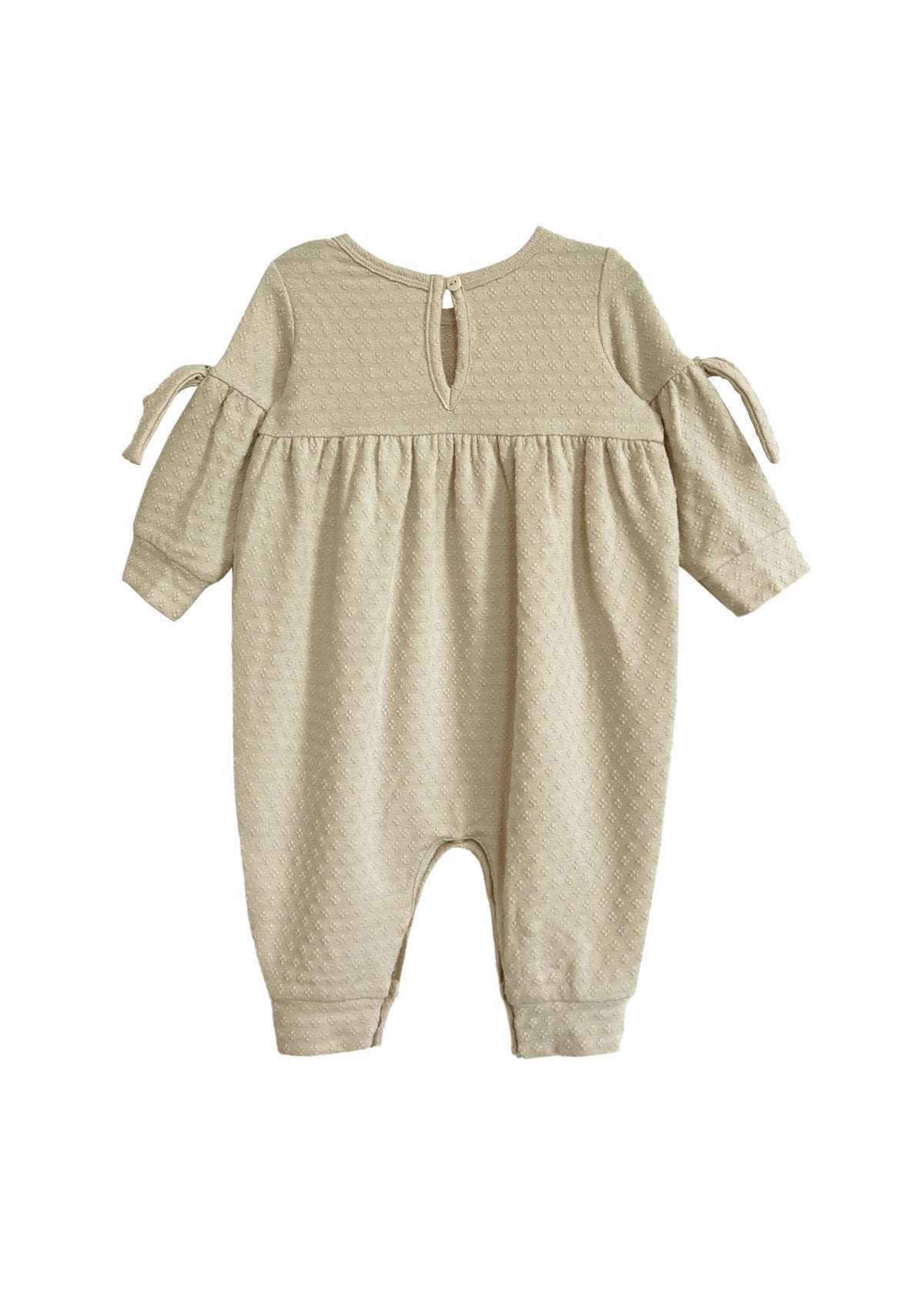 The Cinnamon Sugar Romper by Mabel and Honey is a beige, long-sleeve baby girl romper with textured fabric, a gathered waist, bow-tied sleeves, back button closure, and cuffed ankles for a sweet and comfy fit.