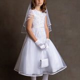 A young girl stands against a plain background, wearing the Lauren Marie Embroidered Bodice and Flower Beaded Waist Dress with gloves, shoes, veil, tiara, and holding a small white purse, looking slightly to the side with a neutral expression.