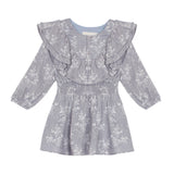 The Frost Rayon Dress by Mabel + Honey is a light purple, long-sleeve dress for little girls featuring a white wildflower print, ruffled shoulders, and a smocked waist. With its round neckline and flowy skirt, this dress is perfect for any special occasion.