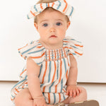 A baby wearing a Mabel and Honey Hermosa Headband and a soft cotton striped romper sits on the floor against a white background, gazing at the camera with a neutral expression.