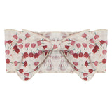The Tulip Fields Headband by Mabel and Honey features a wide, cream cotton band with a red floral pattern, a large center bow, and an elastic back. The fabric is slightly textured and 100% cotton.