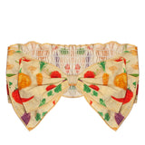 The Garden Party Headband by Mabel and Honey is a cotton bow headband with an elastic band, showcasing a vibrant veggie print of carrots, beets, and greens on beige—a cute and playful hair accessory for babies.
