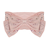 The It's a Party Headband by Mabel and Honey features a wide, sheer pink band with a large central bow, embellished with multicolored glitter dots and subtle sparkles for a soft, delicate look.