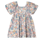 The Flower Mae Floral Dress by Mabel and Honey is a vintage-inspired girl’s dress with puffed short sleeves, a gathered skirt, and a colorful floral print on a blue background.