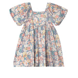 The Flower Mae Floral Dress by Mabel and Honey is a vintage-inspired girl’s dress with puffed short sleeves, a gathered skirt, and a colorful floral print on a blue background.