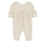 The Mabel and Honey Breakfast in Bed Romper is a cream-colored baby girls’ piece with a green floral print, ruffled sleeves, and gathered fabric for a soft, vintage-inspired look.