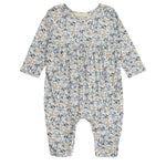 The Mabel and Honey Hazelnut Romper is a long-sleeved baby girl romper with a gathered waist and a blue, beige, and gray floral print, shown flat on a white background.
