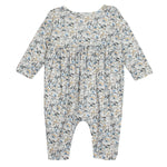 The Hazelnut Romper by Mabel and Honey is a long sleeve baby girl outfit with blue, beige, and green florals on white, gathered chest fabric, and closed feet.