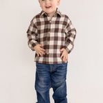A smiling young boy stands against a plain background, wearing the Beckett and Bear S'mores Brothers Top, paired with blue jeans and brown shoes.
