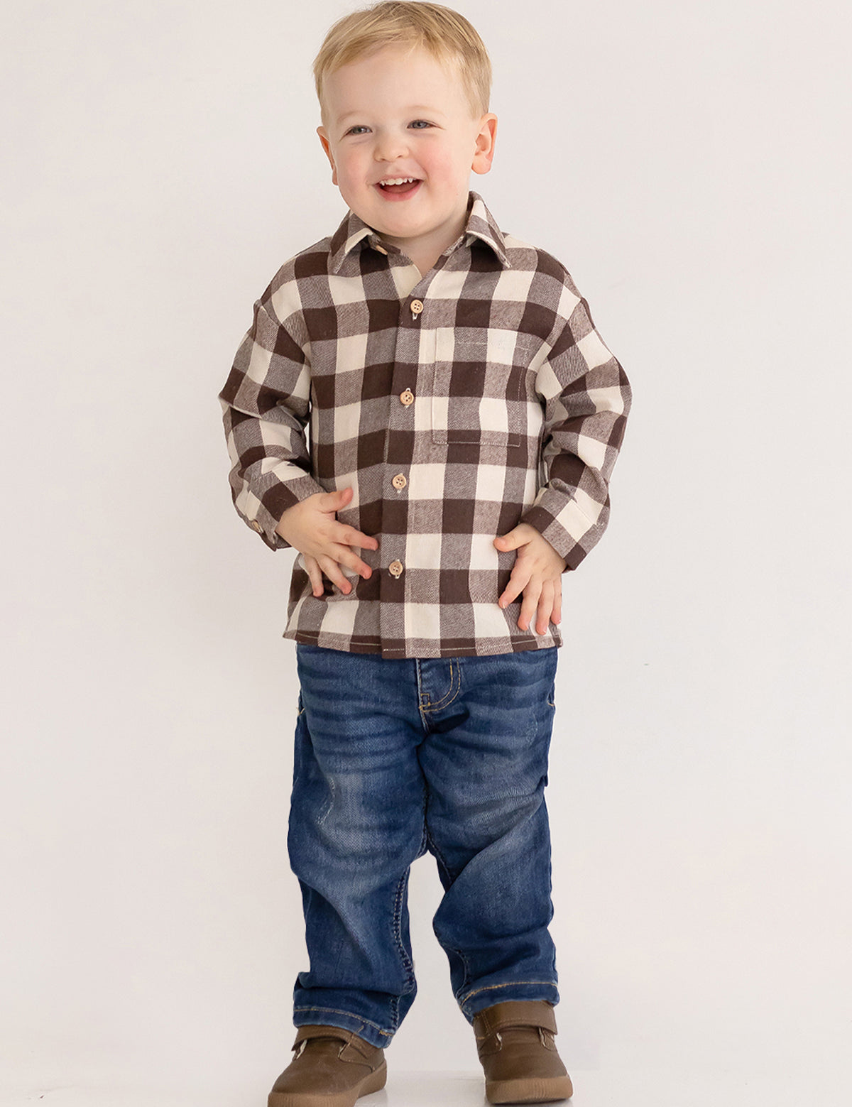 A smiling young boy stands against a plain background, wearing the Beckett and Bear S'mores Brothers Top, paired with blue jeans and brown shoes.
