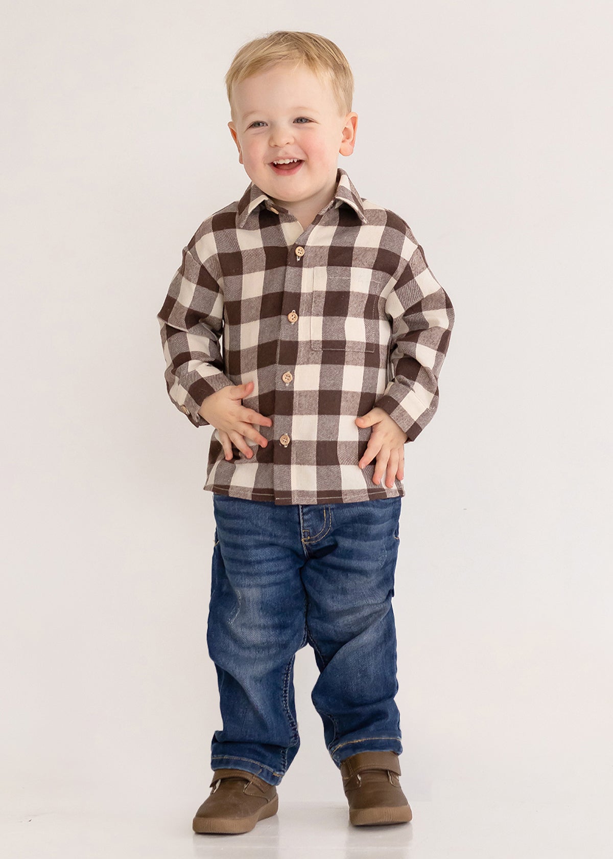 A smiling young boy stands against a plain background, wearing the Beckett and Bear S'mores Brothers Top, paired with blue jeans and brown shoes.