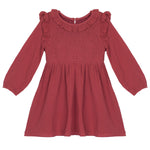 The Mabel and Honey Autumn Dress Red is a children’s knee-length, long-sleeve dress with shoulder ruffles and a smocked bodice, finished with a round neckline.