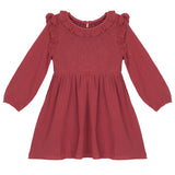 The Mabel and Honey Autumn Dress Red is a children’s knee-length, long-sleeve dress with shoulder ruffles and a smocked bodice, finished with a round neckline.