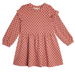 The Red Velvet Dress by Mabel and Honey features long sleeves, ruffled shoulders, a gathered skirt, and playful red polka dots for a charming, feminine look.