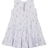 The Tiny Tulip Drop Waist Dress by Mabel and Honey is a sleeveless white girl's dress with a flared, tiered skirt, pink tulip print with green stems, and a teardrop button closure at the back neckline for easy dressing.