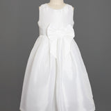 The Taffeta Bow Communion Dress w/ Beaded Pearl Neckline by Mabel and Honey is a sleeveless white girls’ dress with a full skirt, pearl-trimmed neckline, and large waist bow, shown on a dress form against a plain gray background.