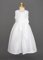 The Taffeta Bow Communion Dress w/ Beaded Pearl Neckline by Mabel and Honey is a sleeveless white girls’ dress with a full skirt, pearl-trimmed neckline, and large waist bow, shown on a dress form against a plain gray background.