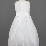 The Mabel and Honey Taffeta Bow Communion Dress features a sleeveless white design, full taffeta skirt, large back bow, and a beaded pearl neckline, displayed on a dress form against a gray background.