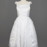 The Mabel and Honey Chiffon Ruffle and Satin Flower Girl Dress features hand-beaded embellishments, ruffle cap sleeves, and a layered skirt, shown on a mannequin against a gray background.