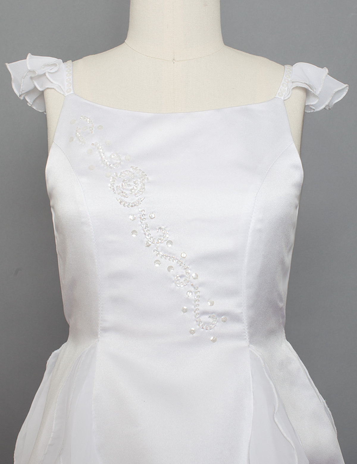 The Mabel and Honey Chiffon Ruffle and Satin Flower Girl Dress features ruffle cap sleeves and hand beaded embellishments, displayed on a mannequin against a gray background.