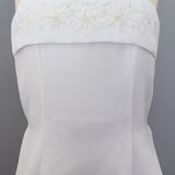 The Mabel and Honey Satin A-Line Communion Dress features a sleeveless design with thin straps, a straight neckline, and hand-beaded embellishments for an elegant, delicate look.