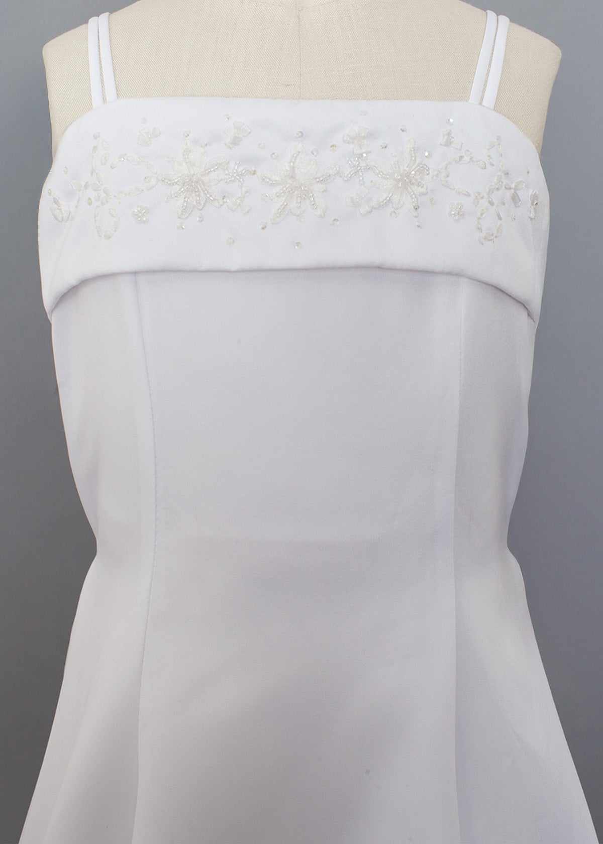 The Mabel and Honey Satin A-Line Communion Dress features a sleeveless design with thin straps, a straight neckline, and hand-beaded embellishments for an elegant, delicate look.