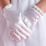 A person wearing Lauren Marie’s Pearl Cuff Gloves—white gloves adorned with elegant pearl beads and shiny cuffs—stands with hands gently clasped.