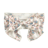 The Sadie Hair Accessory by Mabel and Honey is a wide white fabric headband with an oversized bow, decorated with a delicate blue and pink floral pattern and green stems.