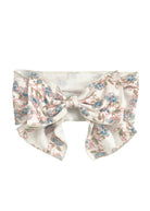 The Sadie Hair Accessory by Mabel and Honey is a wide white fabric headband with an oversized bow, decorated with a delicate blue and pink floral pattern and green stems.