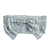 The Georgina Hair Accessory by Mabel and Honey is a light blue and white ruffled headband with a large decorative bow, featuring floral and striped patterns—an adorable choice for baby girls.