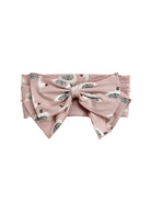 The Ducky in Pink Hair Accessory by Mabel and Honey is a pink headband with an oversized bow, decorated with a playful pattern of small white birds featuring black and brown details.