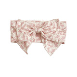 The Primrose Hair Accessory by Mabel and Honey features a wide, light pink fabric with a delicate floral print and a large, structured pink botanical bow at the front.