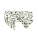 The Lillian Hair Accessory by Mabel and Honey is a vintage-inspired white fabric floral bow with teal patterns, two wide tails, a large central knot, and a textured look for added charm.
