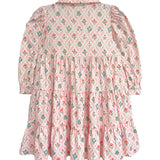 The Dixie Pink Floral Dress by Mabel and Honey features a vintage-inspired tiered silhouette with long sleeves, a collar, and gathered panels for a ruffled pink skirt accented with green and red floral designs.