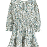 The Brooklyn Floral Dress by Mabel and Honey is a girls' knee-length dress in green, blue, and brown floral on white with long sleeves, a gathered waist, ruffled hem, and button-back closure.
