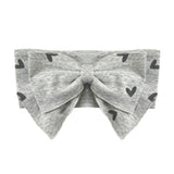 The Mabel and Honey Heartfelt Hair Accessory is a gray baby headband with a bow and black heart print, shown on a white background.