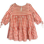 The Tis’ the Season Dress by Mabel and Honey is a loose-fitting girls’ holiday dress featuring red and white gingham, long sleeves with cuff ties, a tiered skirt, and a round neckline with back button keyhole.