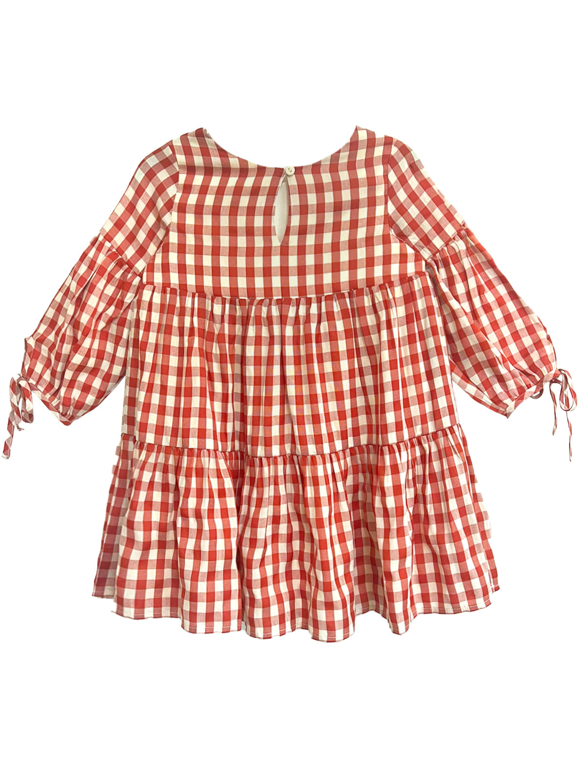 The Tis’ the Season Dress by Mabel and Honey is a loose-fitting girls’ holiday dress featuring red and white gingham, long sleeves with cuff ties, a tiered skirt, and a round neckline with back button keyhole.