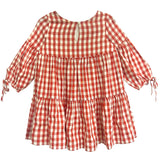 The Tis’ the Season Dress by Mabel and Honey is a loose-fitting girls’ holiday dress featuring red and white gingham, long sleeves with cuff ties, a tiered skirt, and a round neckline with back button keyhole.