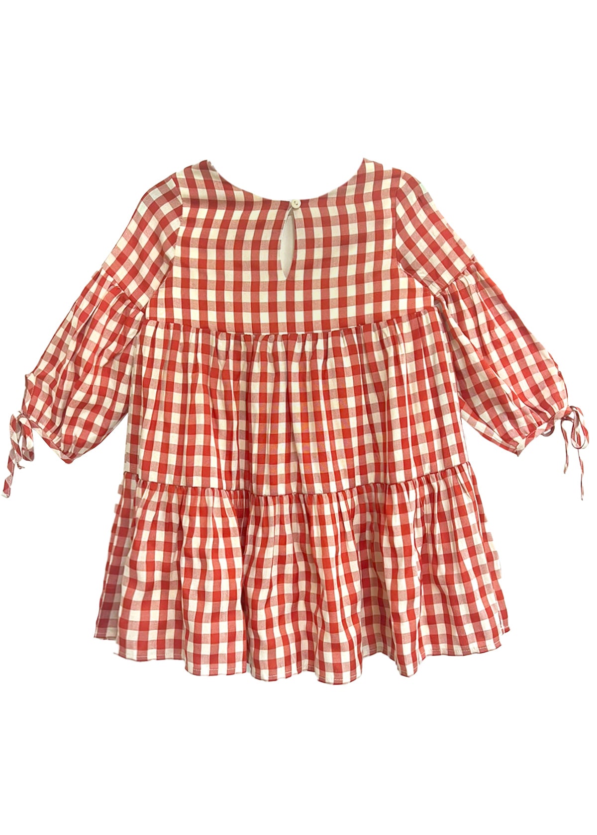 The Tis’ the Season Dress by Mabel and Honey is a loose-fitting girls’ holiday dress featuring red and white gingham, long sleeves with cuff ties, a tiered skirt, and a round neckline with back button keyhole.