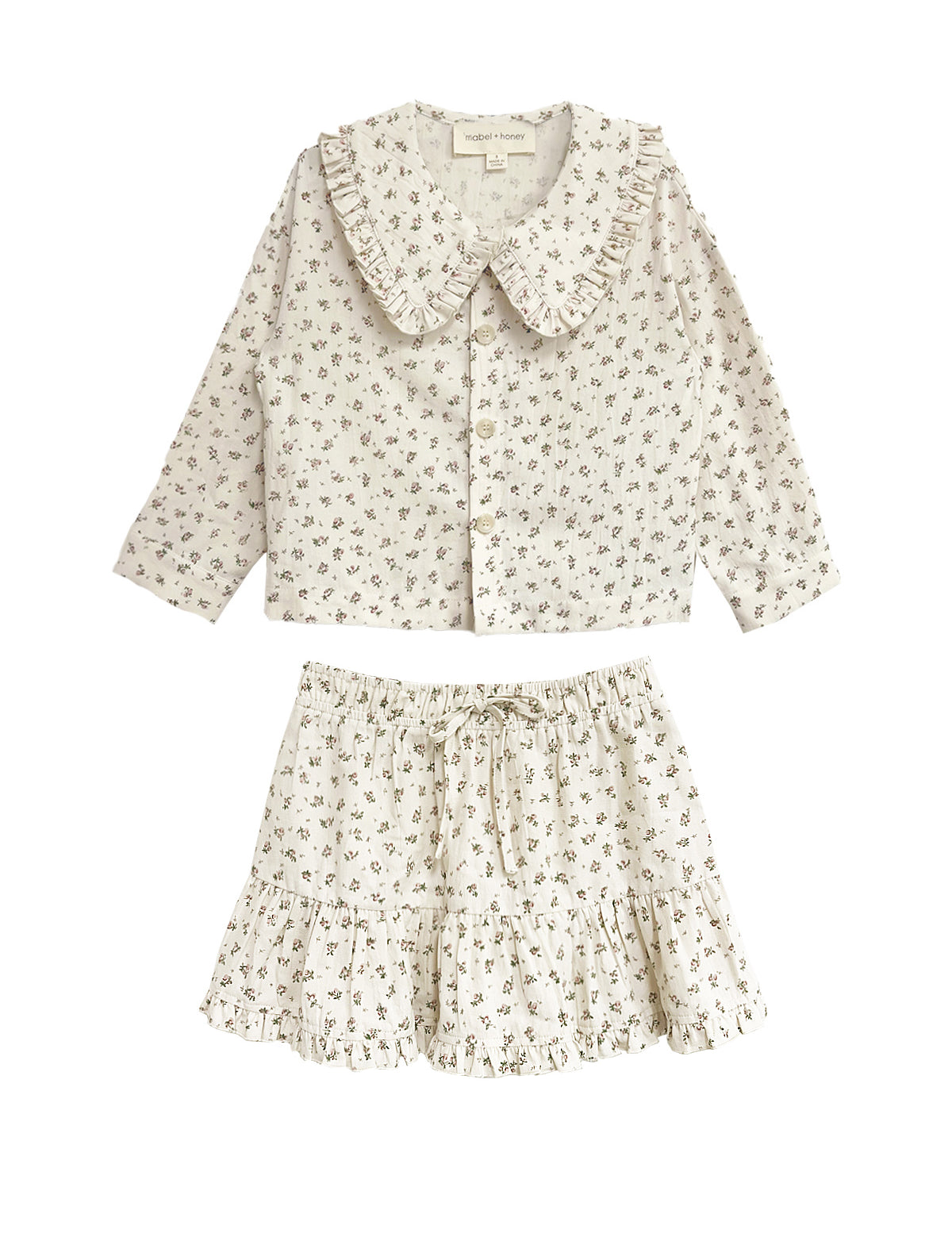 The Juliette Two Piece Set by Mabel and Honey is a charming girls’ outfit with a ruffled-collar button-up top and drawstring skirt, both in lightweight fabric with a delicate floral print.
