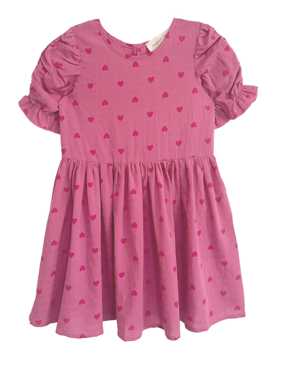 The Mabel and Honey Perfect in Pink Hearts Short Sleeve Dress is a girls’ pink dress with puffed ruffled sleeves, a flared skirt, and a sweet pattern of small, darker pink hearts.