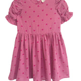 The Mabel and Honey Perfect in Pink Hearts Short Sleeve Dress is a girls’ pink dress with puffed ruffled sleeves, a flared skirt, and a sweet pattern of small, darker pink hearts.