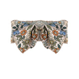 The Riley Hair Accessory by Mabel and Honey is a baby girl bow with orange, blue, and white flowers plus green leaves on beige. It features a gathered center and pointed ends for added charm.