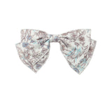 The Mabel and Honey Meadow Hair Accessory is a lightweight fabric bow for baby girls, featuring brown and light blue floral patterns on white. Shown against a plain white backdrop.