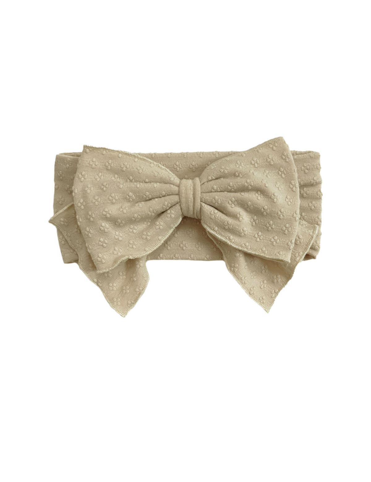 The Cinnamon Sugar Hair Accessory by Mabel and Honey is a beige fabric headband with a large bow and subtle textured floral pattern, adding elegant charm to any outfit.
