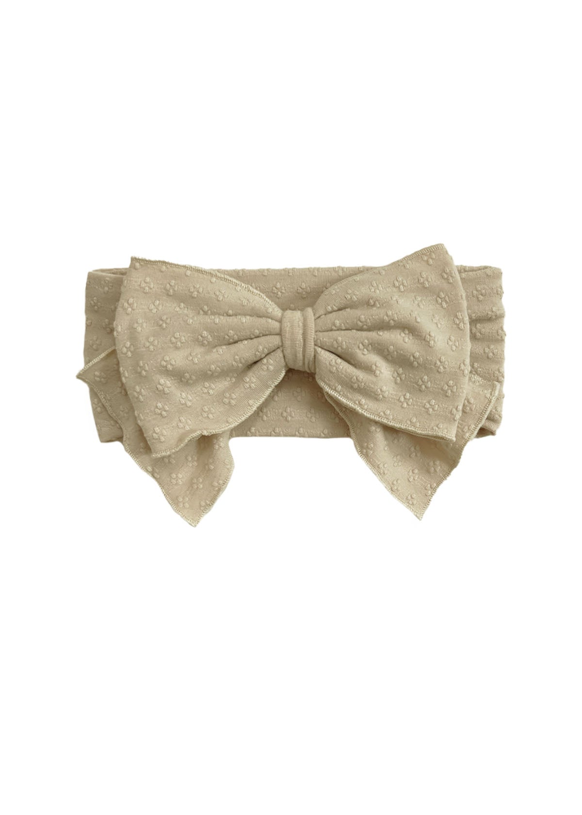The Cinnamon Sugar Hair Accessory by Mabel and Honey is a beige fabric headband with a large bow and subtle textured floral pattern, adding elegant charm to any outfit.