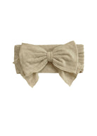 The Cinnamon Sugar Hair Accessory by Mabel and Honey is a beige fabric headband with a large bow and subtle textured floral pattern, adding elegant charm to any outfit.