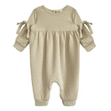 The Cinnamon Sugar Romper by Mabel and Honey is a beige textured baby girl's romper with long sleeves, gathered waist, sleeve bows, and a footless design—perfect for cozy everyday comfort.